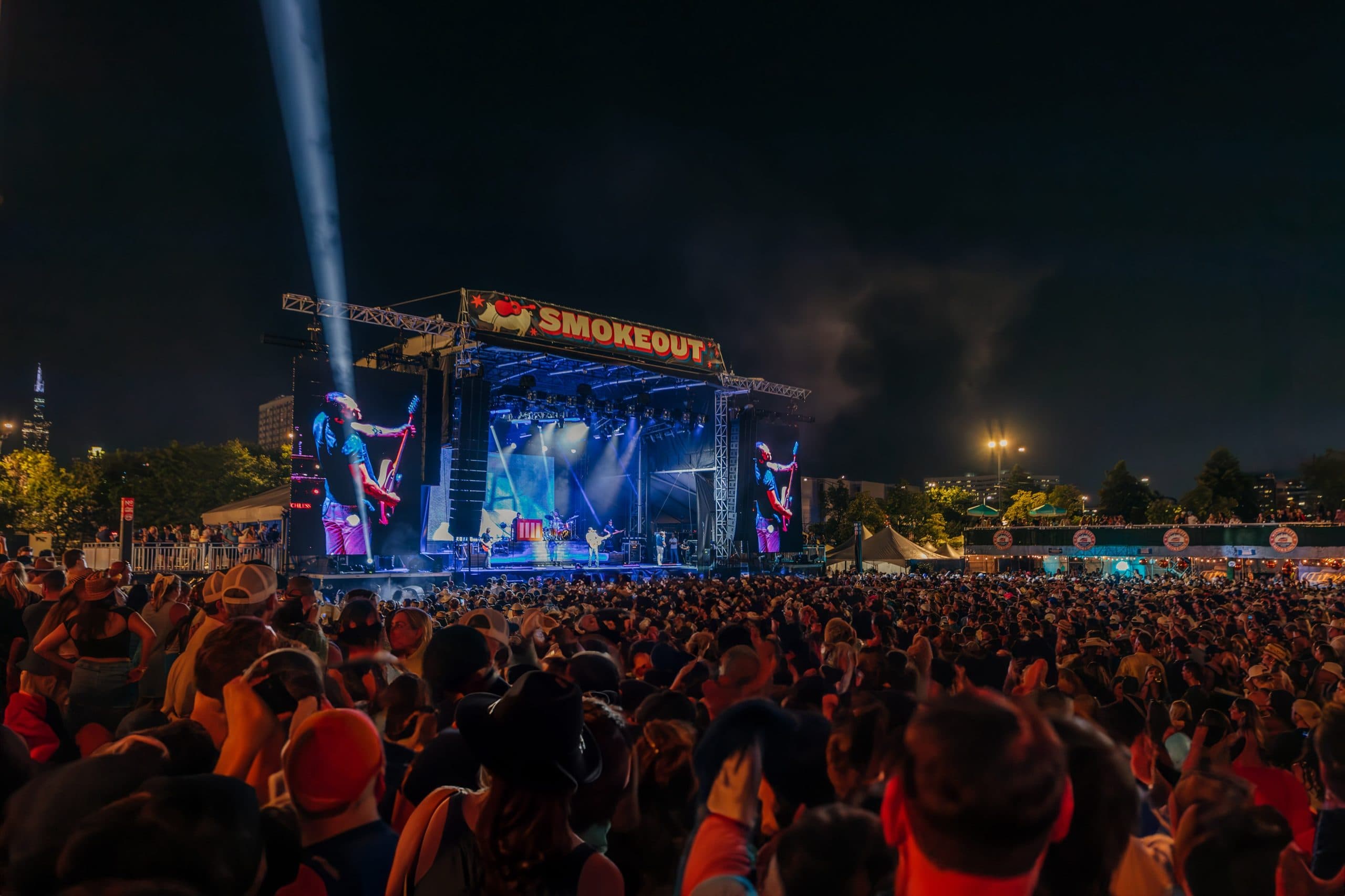 large shot of a the crowd focusing on a single woman sitting on the shoulders of a man so she can see over the crowd