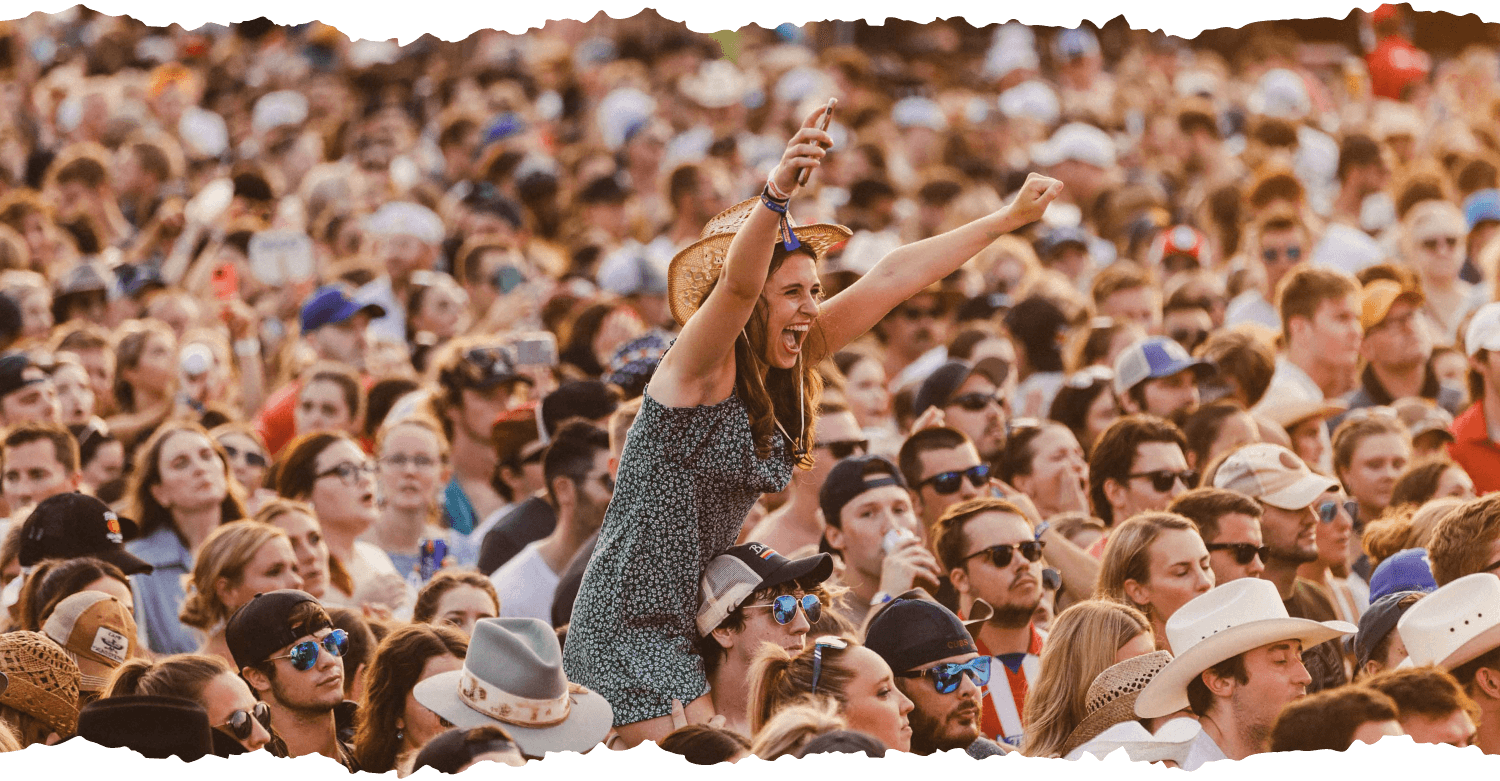 crowd shot focusing on a woman sitting on a mans shoulders so she can see over the crowd